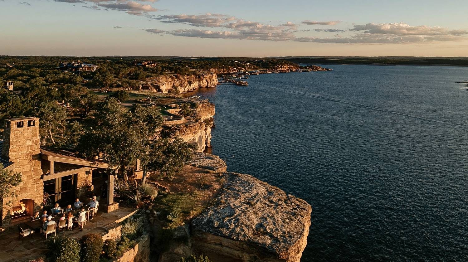 Family gathered around an outdoor stone fireplace on a cliff overlooking Possum Kingdom Lake at golden hour